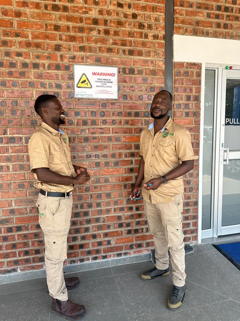 Two Sentinel staff at a building entrance, the CCTV sign on the wall beside them
